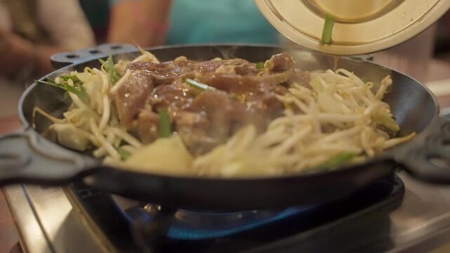 Aromatic sauce pouring over sizzling lamb and bean sprouts while preparing a traditional Jingisukan grilled mutton dish, a local specialty from Hokkaido, Japan, cooked on a tabletop stove