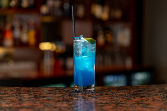 View of a refreshing blue cocktail served in a tall glass with ice and a lime wedge on a polished bar counter in Asker, Akershus, Norway.