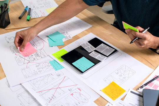 UX UI designer working on wireframes for a website and mobile app prototype, surrounded by sketches of user-flow and design tools, in concept of website and mobile application design concept.