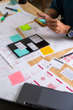 UX UI designer working on wireframes for a website and mobile app prototype, surrounded by sketches of user-flow and design tools, in concept of website and mobile application design concept.