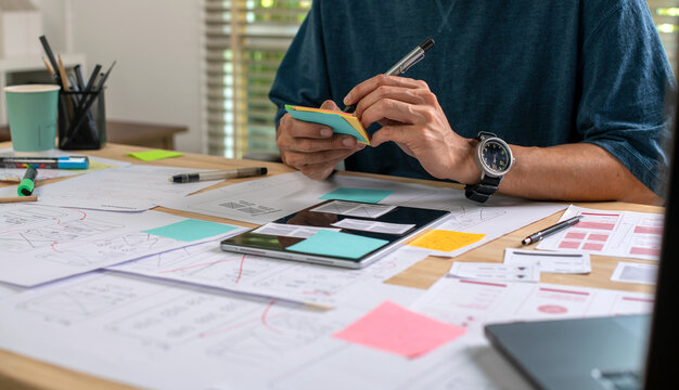 UX UI designer working on wireframes for a website and mobile app prototype, surrounded by sketches of user-flow and design tools, in concept of website and mobile application design concept.