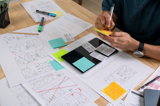 UX UI designer working on wireframes for a website and mobile app prototype, surrounded by sketches of user-flow and design tools, in concept of website and mobile application design concept.