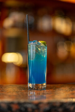 View of a refreshing blue cocktail in a tall glass with ice cubes and a lime wedge on a bar counter in Asker, Akershus, Norway.
