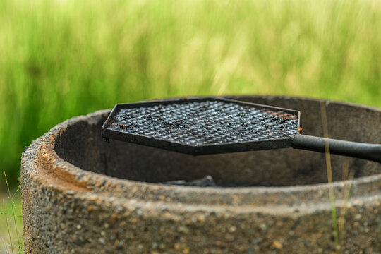 Black waffle iron resting over rustic outdoor fire pit.