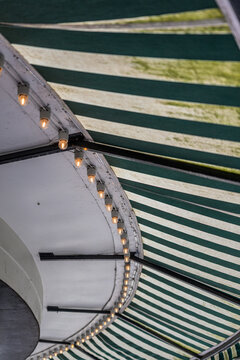 Curved striped amusement park canopy with glowing warm bulbs.