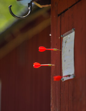 Red darts stuck in weathered wooden wall during outdoor game.