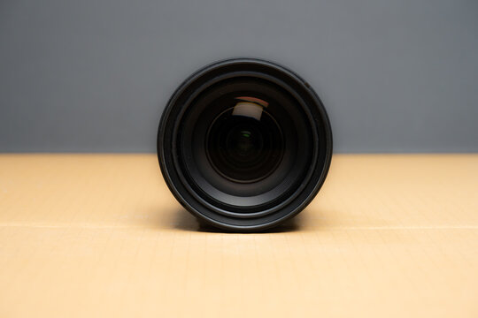 Camera zoom lens lying on cardboard surface front view.