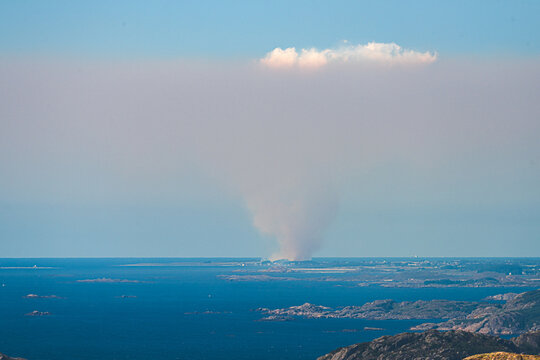Distant smoke cloud above sea and rocky coastal islands.