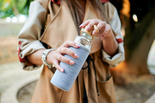Woman opening reusable glass water bottle outdoors