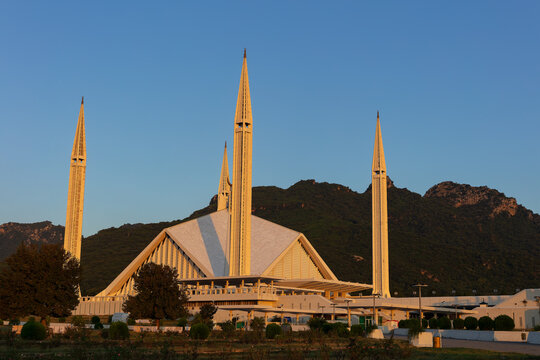 View of Faisal Masjid with its triangular architecture and four slender minarets set against the Margalla Hills during golden hour in Islamabad, Islamabad Capital Ter, Pakistan.