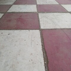 Fototapeta premium Classic alternating checkerboard pattern outdoor courtyard floor tiles painted in faded red and white contrasting visual colors
