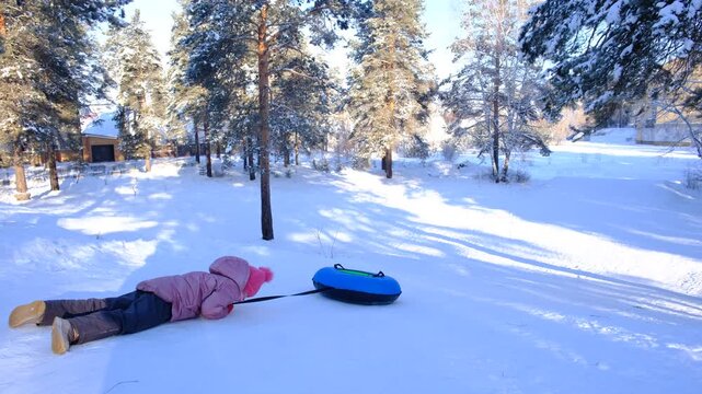 Family having fun outdoors in winter: girl on a toboggan hill, tubing, snowy landscape. Joyful winter scene, atmosphere is playful and full of humor, snow‑covered trees and  wintry northern landscape 