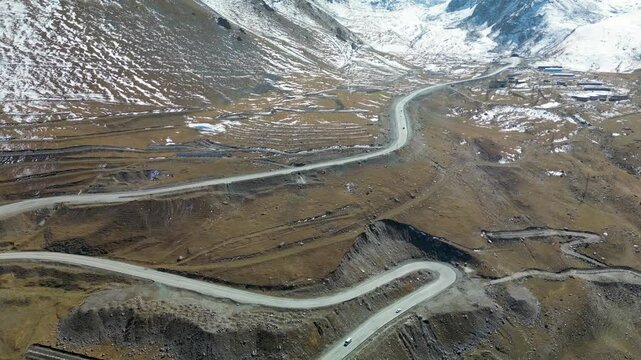 Aerial drone footage of Too-Ashuu Pass in Kyrgyzstan, featuring early autumn snow, moving traffic and the winding Bishkek&ndash;Osh highway crossing the high-altitude Tian Shan mountains.