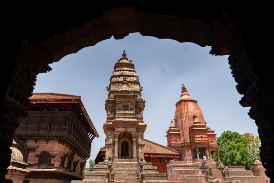 View of the historic stone temples at Bhaktapur Durbar Square with intricate carvings and traditional brick architecture under a clear blue sky in Bhaktapur, Bagmati Province, Nepal.