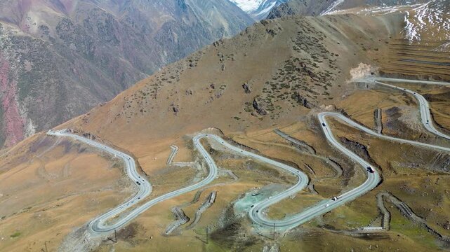 Aerial drone footage overlooking Too-Ashuu Pass in Kyrgyzstan, featuring the winding Bishkek&ndash;Osh highway with vehicles crossing the rugged Tian Shan mountains.