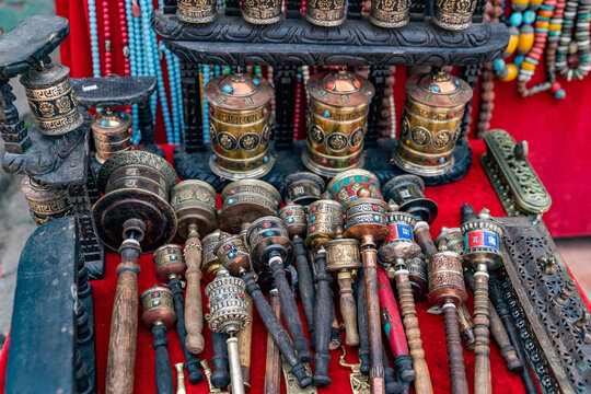 View of traditional Tibetan prayer wheels with intricate metalwork and turquoise inlays displayed on a red cloth at Bhaktapur Durbar Square in Bhaktapur, Bagmati Province, Nepal.