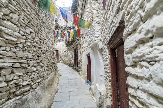 View of the narrow stone-walled alleyway in Marpha decorated with colorful prayer flags in Jomsom, Gandaki Province, Nepal.