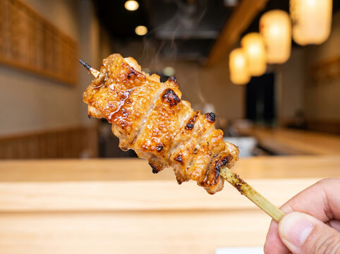 Hand holding a grilled glazed yakitori skewer in a Japanese restaurant