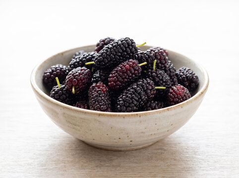 Fresh dark ripe mulberries served in a ceramic bowl on a wooden surface
