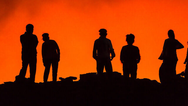 View of silhouetted people standing on the rim of the Erta Ale volcano with glowing lava in the background in Zone 2, Afar, Ethiopia.