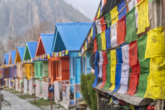 View of Alpine Home with colorful wooden cabins and vibrant Tibetan prayer flags in the mountainous landscape of Tanki Manang, Gandaki Province, Nepal.
