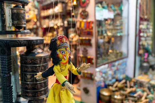 Kathmandu, Nepal - 04 April 2025: View of a traditional Nepali marionette puppet displayed in a shop in Thamel, with prayer wheels and brass handicrafts in the background.