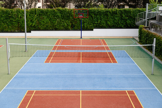 Basketball hoop and tennis nets on a sports court in a green area