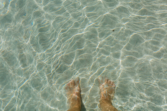 upper view of person bare feet standing in the sea on the sand under direct sun