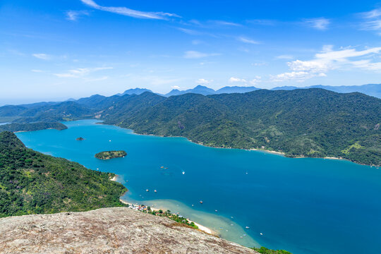 View of Mamangua Bay with lush green mountains, turquoise waters, small islands, and boats under a clear blue sky in Paraty, State of Rio de Janeiro, Brazil.