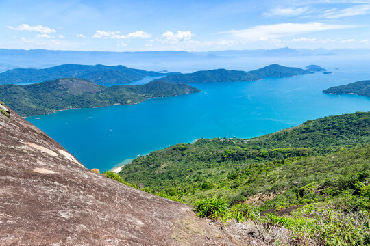 View of Mamangua Bay featuring lush green hills, turquoise waters, and rocky terrain in Paraty, Rio de Janeiro, Brazil.
