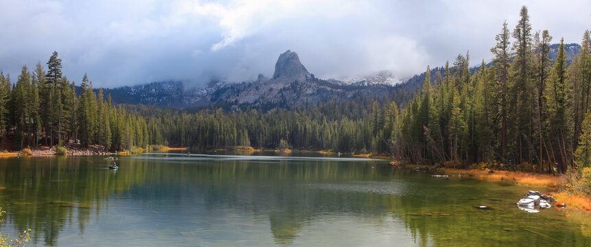 Aerial view of Lake Mary surrounded by dense pine forests and the rugged Crystal Crag peak under a cloudy sky in Mammoth Lakes, California, United States.