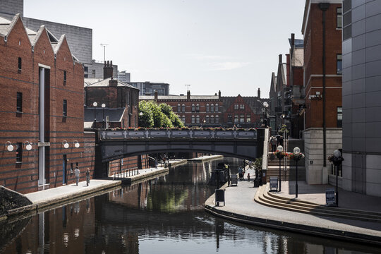 View of the canal network in Birmingham, featuring historic brick buildings, a pedestrian bridge, and walkways along the water in Birmingham, England, United Kingdom.