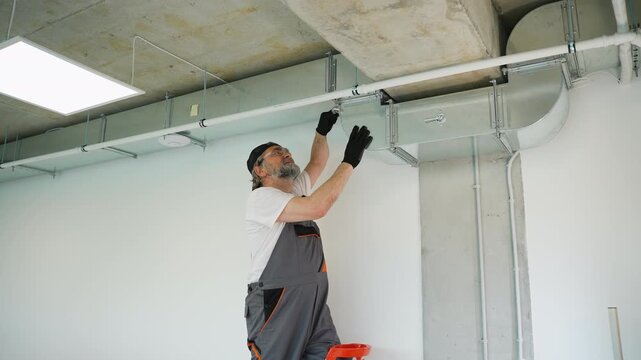 Older hvac technician installing ventilation system ductwork on ceiling