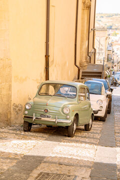 Noto, Italy - 9 July 2026: Vintage green Fiat 600, larger than the 500, parked on a cobblestone street by light yellow stone buildings in Sicily