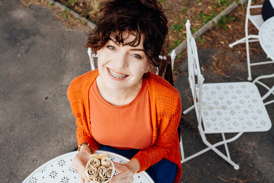 Cheerful middle-aged woman with braces holding rolled ice cream, high angle