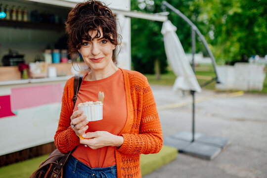 Stylish middle-aged woman holding rolled ice cream outside food truck with copy space