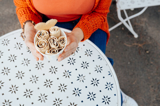 Overhead view of woman holding rolled ice cream above white outdoor table