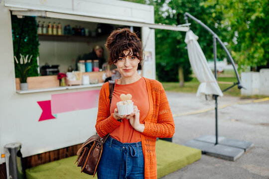 Confident middle-aged woman presenting rolled ice cream in front of food truck