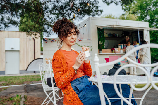 Relaxed middle-aged woman eating rolled ice cream at outdoor food truck cafe