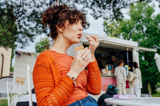 Thoughtful middle-aged woman tasting rolled ice cream beside outdoor food truck