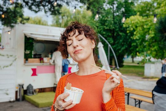 Satisfied middle-aged woman savoring rolled ice cream near outdoor food truck
