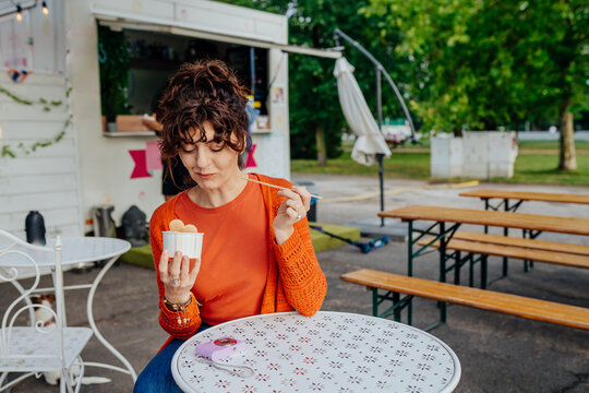 Thoughtful middle-aged woman eating rolled ice cream beside food truck