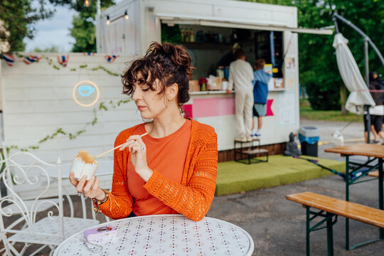 Casual middle-aged woman enjoying rolled ice cream at outdoor street food cafe
