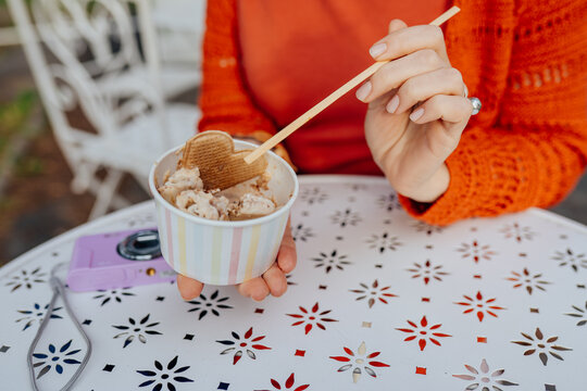 Close-up of woman eating rolled ice cream with wooden stick at outdoor cafe