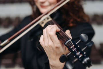 Fototapeta premium violinist outdoors, young beautiful redhead caucasian woman in jacket playing black violin in city park with green grass and trees in sunny summer day, classic music concept, selective focus