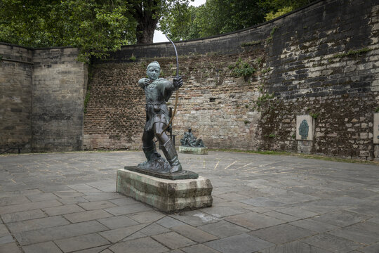 View of the bronze Robin Hood statue in a paved courtyard with a historic stone wall background in Nottingham, England, United Kingdom.
