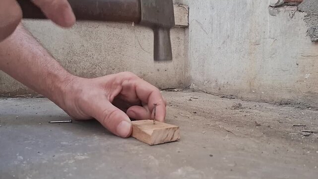 Construction worker hammering a wooden block on concrete surface. Skilled tradesman performing carpentry work for building or renovation projects.