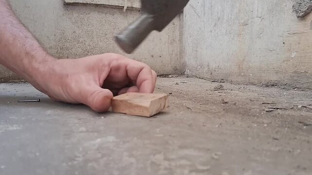 Hand using hammer to level concrete surface. Construction worker installing flooring or pavement.