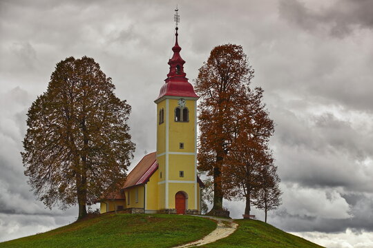 Two autumn-colored linden trees frame the Baroque, XVII c.Saint Thomas church (Cerkev svetega Tomaza) in Gorenji Vrsnik village. Idrija-Slovenia-194