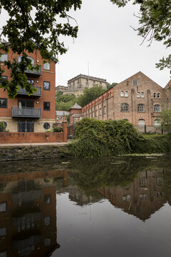 View of Nottingham Castle overlooking historic red brick buildings and a calm canal with reflections in Nottingham, England, United Kingdom.